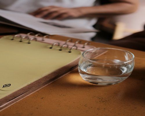 A neat work desk setup with a journal, glasses, and a glass of water, showing a calm lifestyle